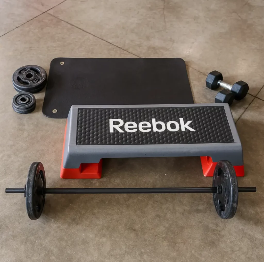 Équipement de body pump complet avec step Reebok, barre de musculation, disques, haltères et tapis, prêt pour une séance de renforcement musculaire en salle.