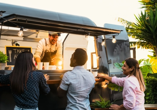 Clients souriants devant le food truck Fitmeal rotisserie, spécialisé en repas sains et rôtisserie mobile, dans une ambiance chaleureuse en plein air.