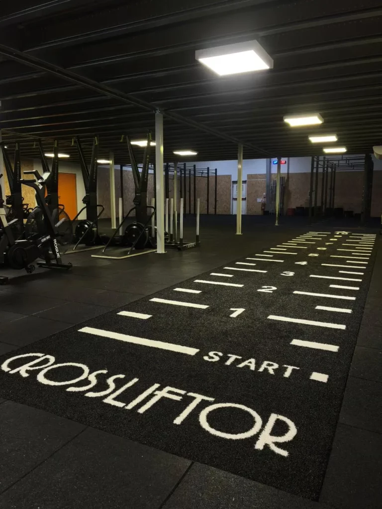 Salle HYROX à Beynost équipée de machines de cardio, zone de sprint avec piste marquée CROSSLIFTOR et espace d'entraînement fonctionnel dédié au cross-training.