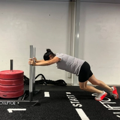 Athlète réalisant un sled push lors d’une séance d'HYROX, concentré sur l’effort, en poussant une luge de force sur piste intérieure.